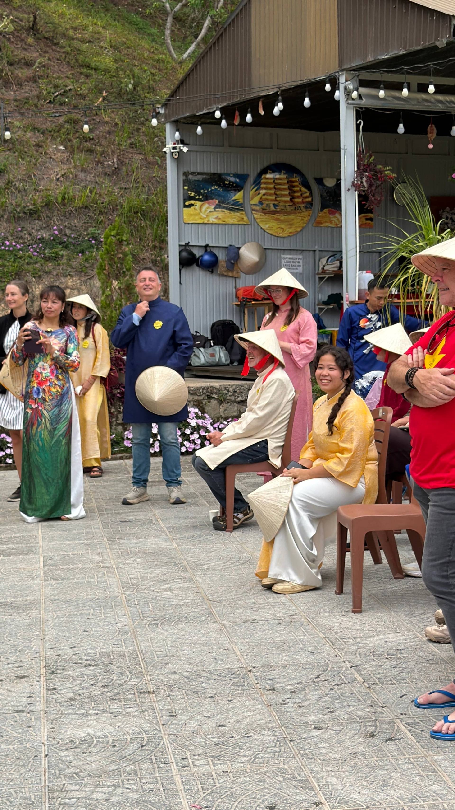 Daytime cultural event in Đà Lạt featuring traditional Vietnamese dress, conical hats, decorative greenery, and participants engaging in activities at a covered outdoor venue.