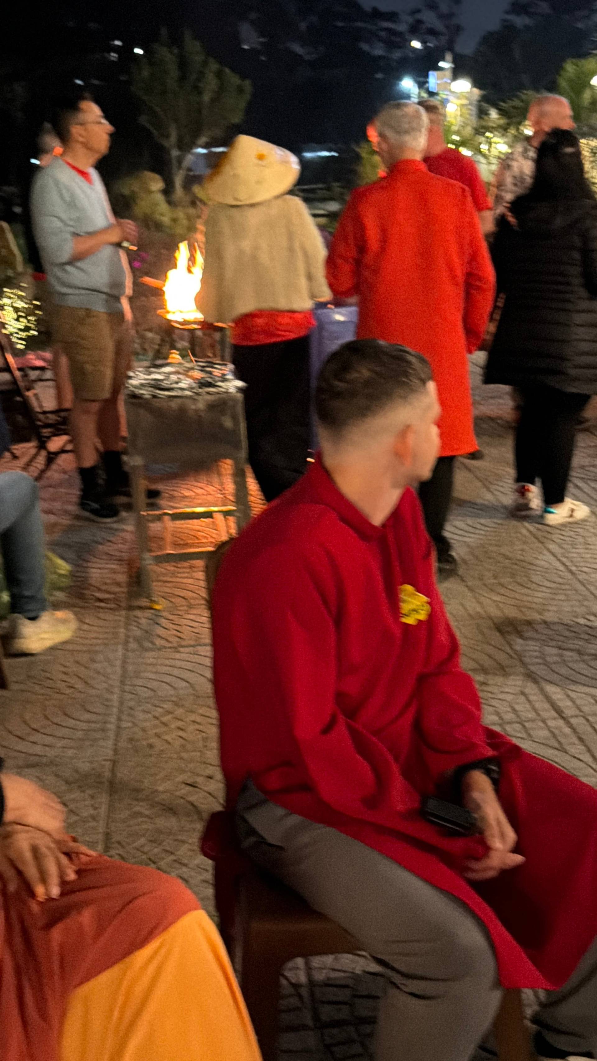 An evening bonfire gathering in Đà Lạt's pine forest with participants in traditional red áo dài celebrating together around a firepit.