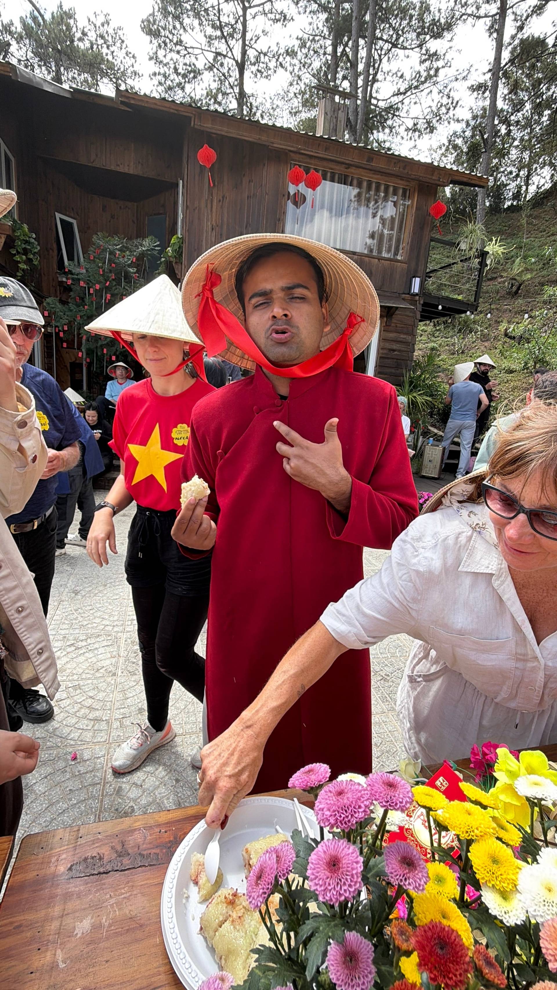 A cultural celebration in Đà Lạt featuring traditional Vietnamese áo dài, conical hats, and Lunar New Year décor with red lanterns and vibrant flowers in a rustic pine-forest setting.