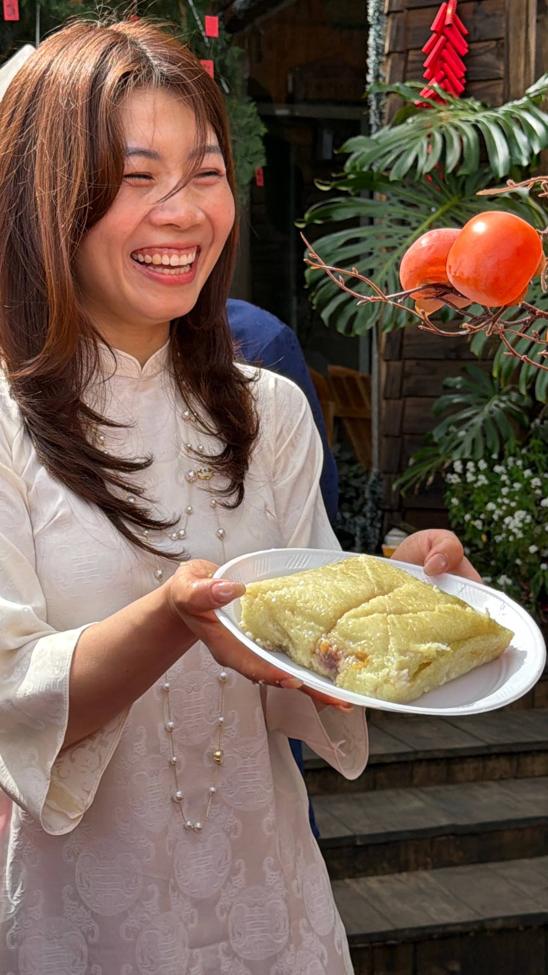 A joyful moment in Đà Lạt showcases traditional Vietnamese cuisine being presented in a festive heritage setting with cultural decorations and flowering plants. The scene celebrates both culinary traditions and cultural pride during Tet celebrations in Vietnam's mountainous highland city.