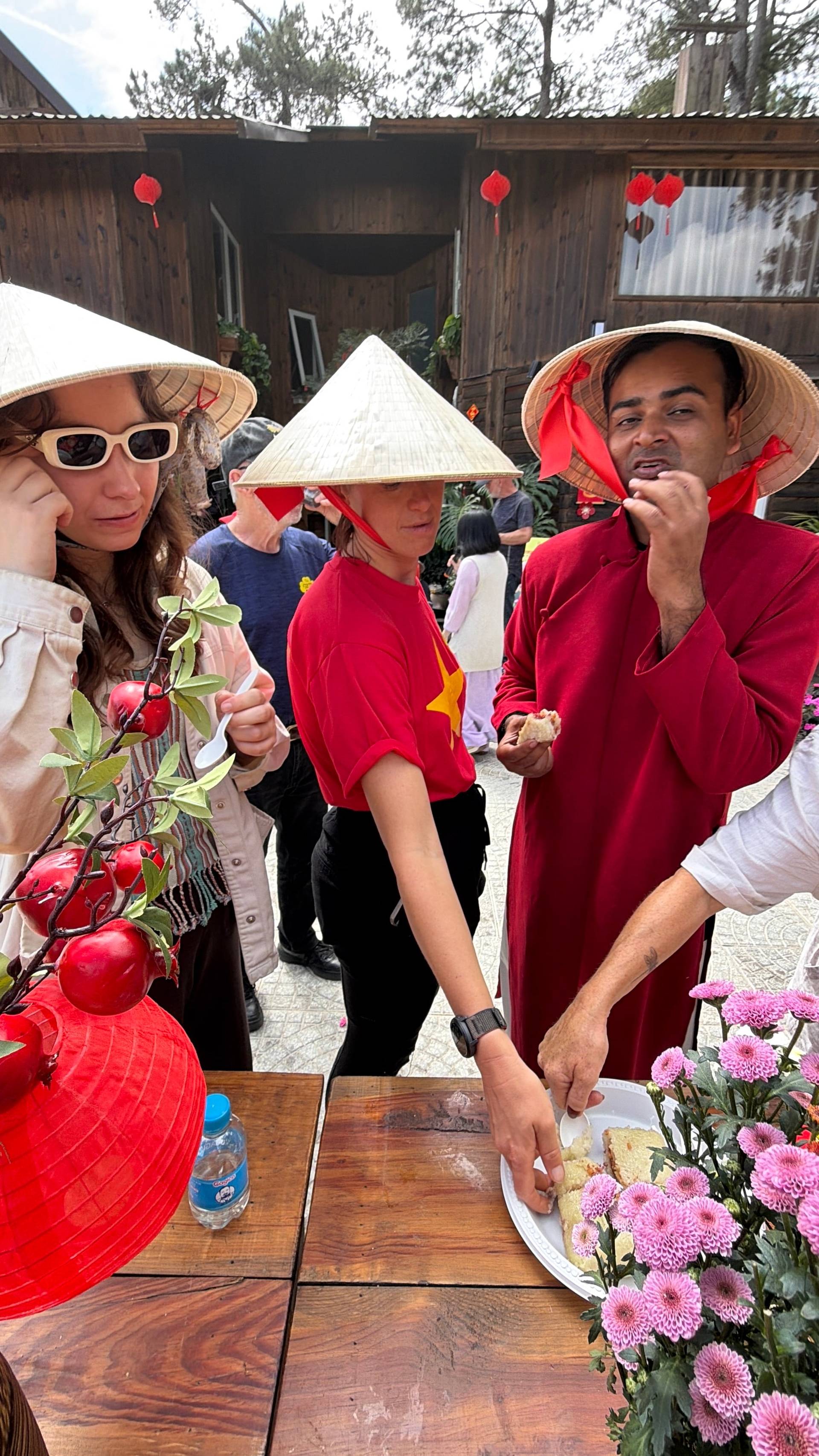 A festive cultural dining scene in Đà Lạt featuring visitors in traditional Vietnamese áo dài sharing food and beverages at a wooden table amid decorative lanterns and fresh flowers. The intimate moment captures authentic Tet celebration customs and heritage food traditions in the mountain city.