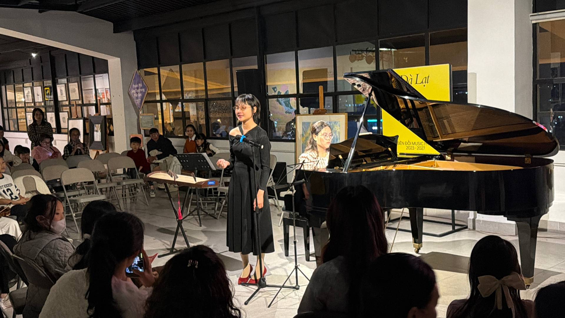 A comprehensive view of an indoor classical music event in Đà Lạt featuring a grand piano performance and engaged audience in a high-rise venue with panoramic city views.