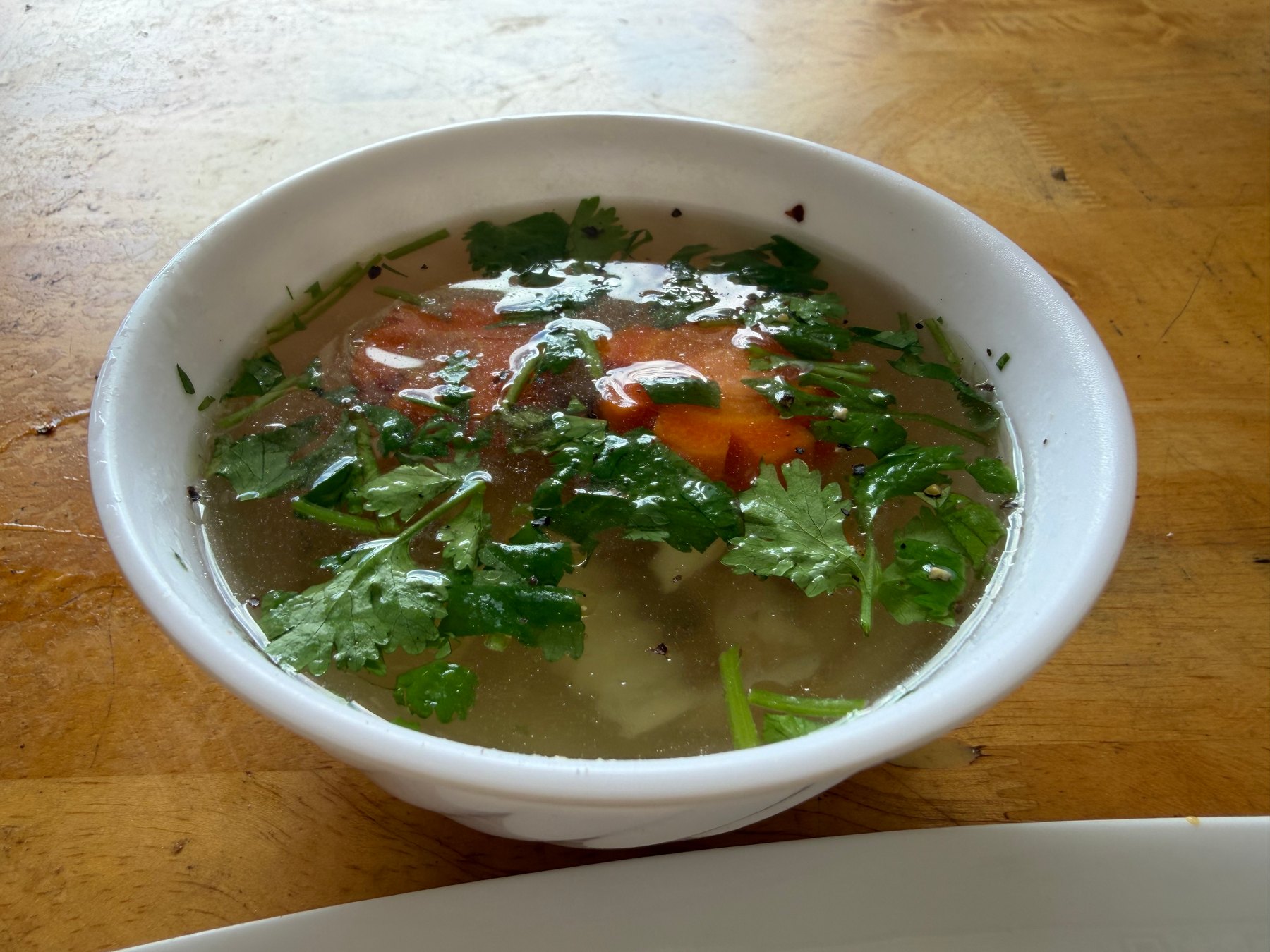 A bowl of clear soup with herbs and vegetables