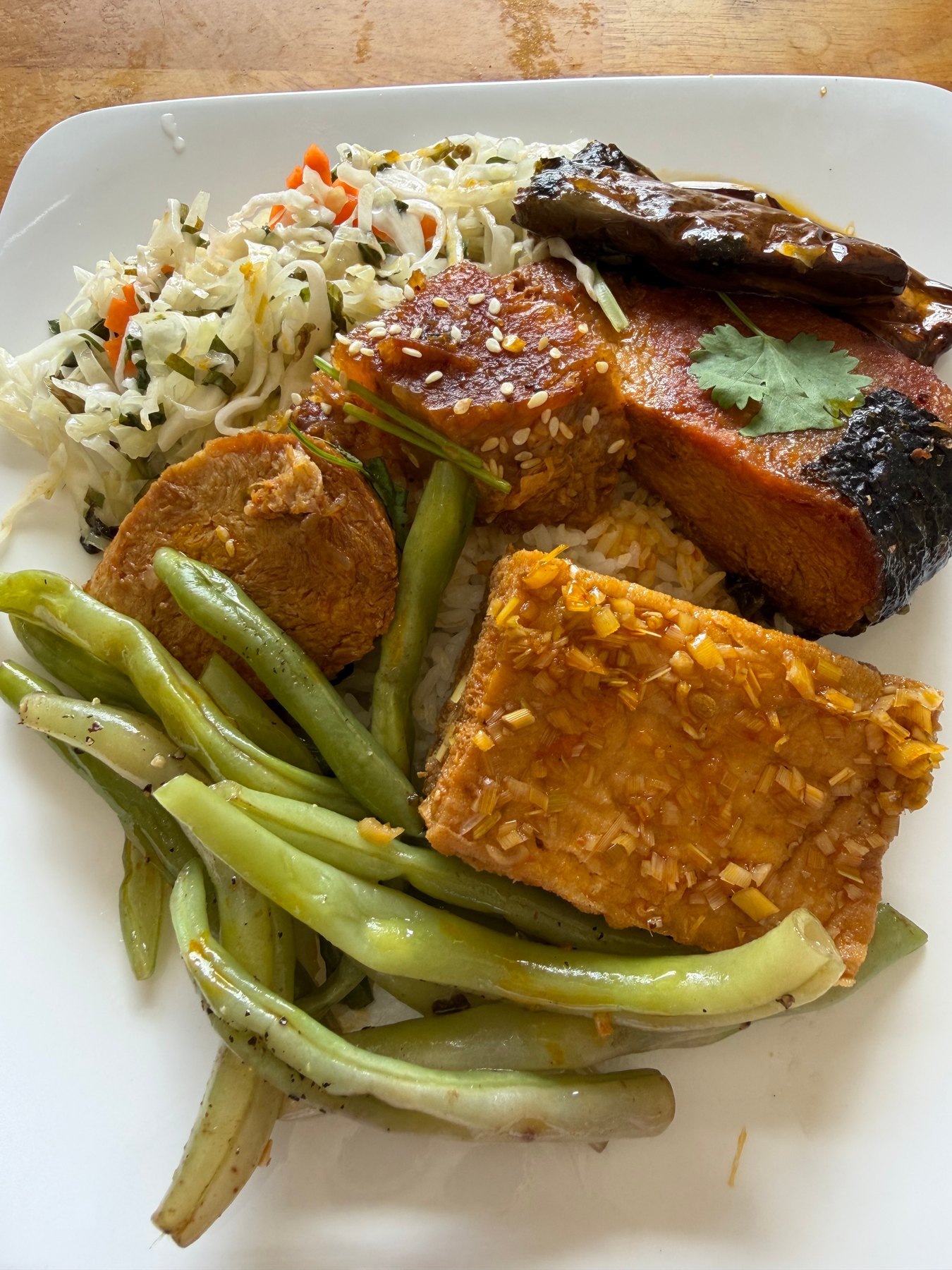 A plate of vegetarian food with rice, green beans, tofu, and other dishes